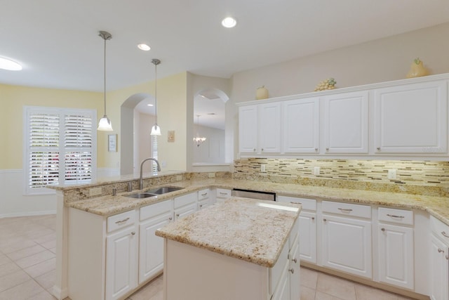 kitchen featuring decorative backsplash, light stone counters, a center island, white cabinetry, and a sink