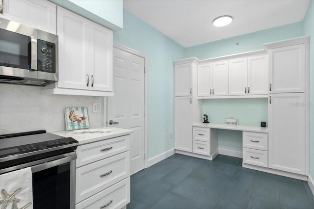 kitchen featuring white cabinets, stainless steel appliances, built in desk, and light countertops