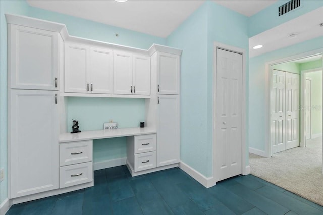 unfurnished office featuring visible vents, built in desk, and baseboards