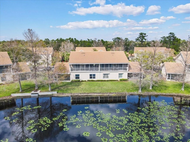 rear view of property with a yard, a water view, a tile roof, and a sunroom