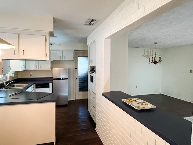 kitchen with white appliances, a sink, visible vents, dark wood-style floors, and dark countertops