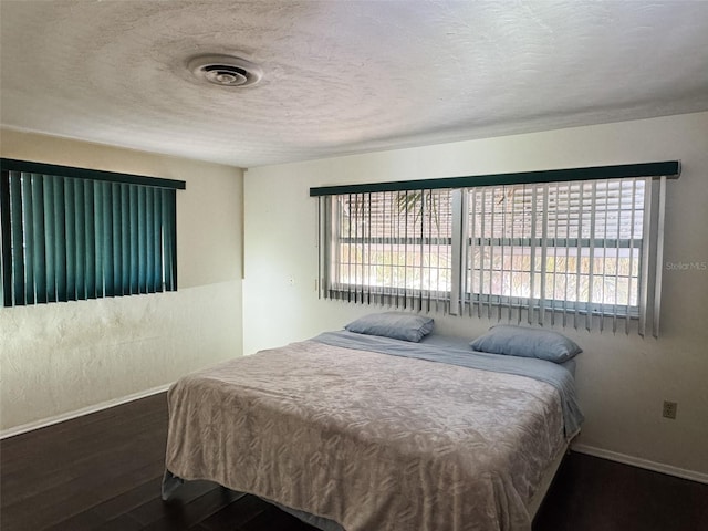 bedroom with a textured ceiling, baseboards, and wood finished floors