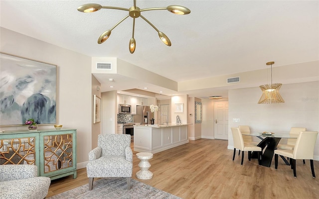 dining room featuring light wood-type flooring, visible vents, a textured ceiling, and baseboards