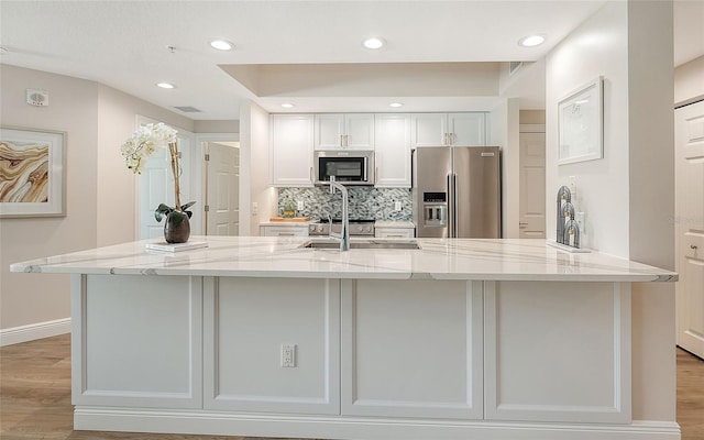 kitchen featuring white cabinets, light stone counters, stainless steel appliances, and a sink