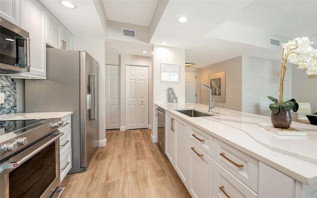 kitchen featuring visible vents, appliances with stainless steel finishes, light stone countertops, white cabinetry, and a sink