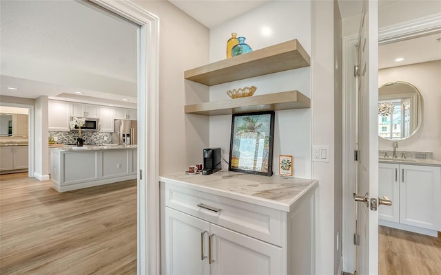 bar featuring appliances with stainless steel finishes, light wood-type flooring, a sink, and backsplash