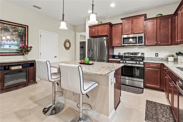 kitchen featuring visible vents, appliances with stainless steel finishes, a kitchen breakfast bar, a center island, and light stone countertops