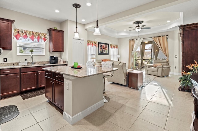 kitchen featuring a kitchen island, open floor plan, a tray ceiling, a sink, and light tile patterned flooring