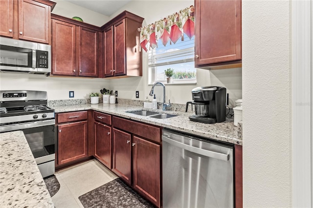 kitchen featuring reddish brown cabinets, light stone counters, light tile patterned floors, stainless steel appliances, and a sink