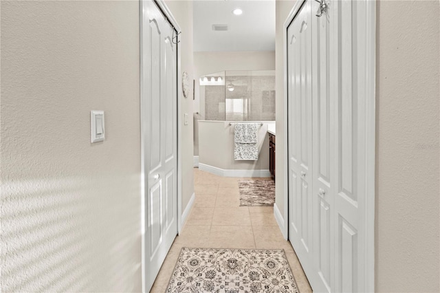 hall featuring light tile patterned flooring, visible vents, and baseboards