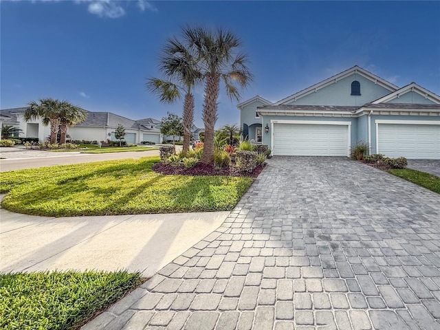 ranch-style house featuring a front yard, decorative driveway, an attached garage, and stucco siding