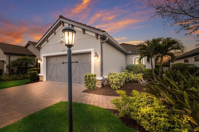 view of front of house featuring an attached garage, a tiled roof, decorative driveway, and stucco siding