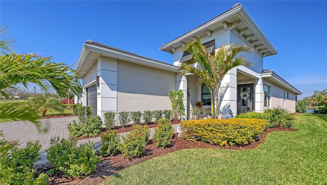 view of front facade with decorative driveway, a front yard, an attached garage, and stucco siding