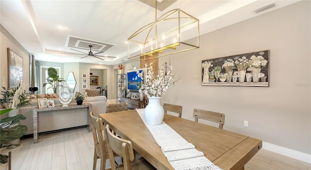 dining space with wood finished floors, visible vents, baseboards, a ceiling fan, and a tray ceiling