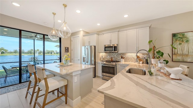 kitchen featuring stainless steel appliances, backsplash, a sink, a kitchen island, and light stone countertops