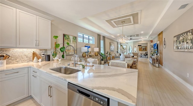 kitchen featuring white cabinets, open floor plan, a tray ceiling, stainless steel dishwasher, and a sink