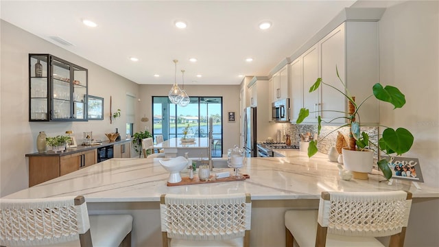 kitchen featuring stainless steel appliances, visible vents, backsplash, light stone countertops, and beverage cooler