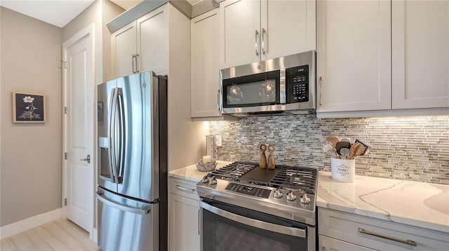 kitchen featuring baseboards, light stone counters, stainless steel appliances, and backsplash