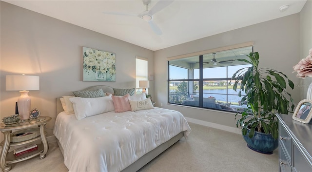 bedroom featuring light carpet, ceiling fan, a water view, and baseboards