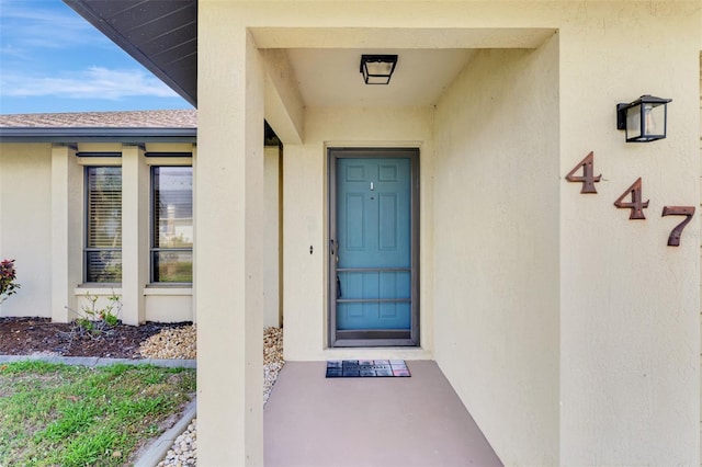 view of exterior entry with a shingled roof and stucco siding