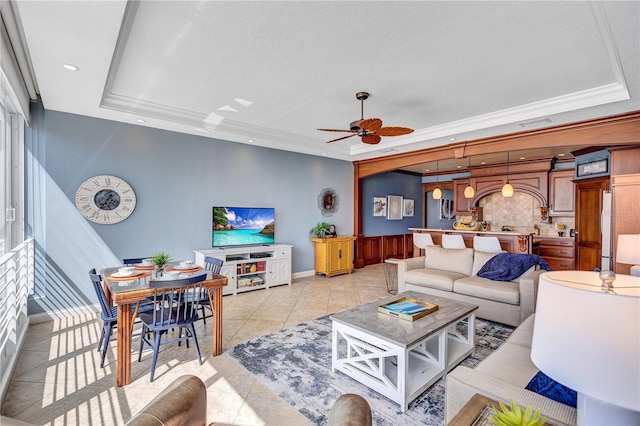 living area featuring a ceiling fan, a tray ceiling, and light tile patterned flooring