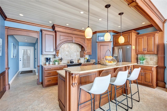 kitchen with a breakfast bar, appliances with stainless steel finishes, decorative backsplash, a center island with sink, and crown molding