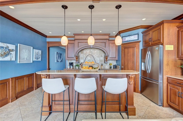 kitchen with brown cabinets, stainless steel fridge with ice dispenser, ornamental molding, light stone countertops, and a kitchen bar