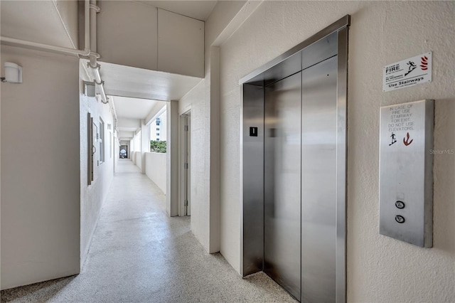 corridor featuring elevator and a textured wall