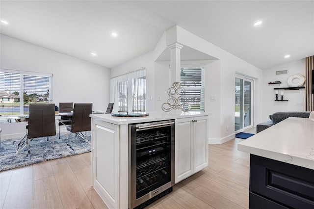 kitchen with light wood-type flooring, lofted ceiling, beverage cooler, and white cabinetry