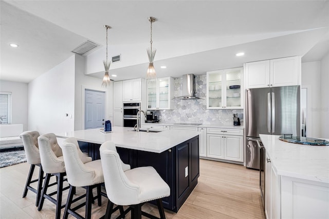 kitchen featuring a center island with sink, lofted ceiling, appliances with stainless steel finishes, a sink, and wall chimney exhaust hood