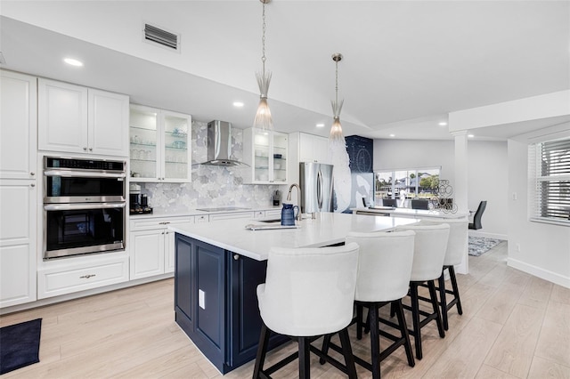 kitchen with visible vents, appliances with stainless steel finishes, light countertops, wall chimney range hood, and a sink