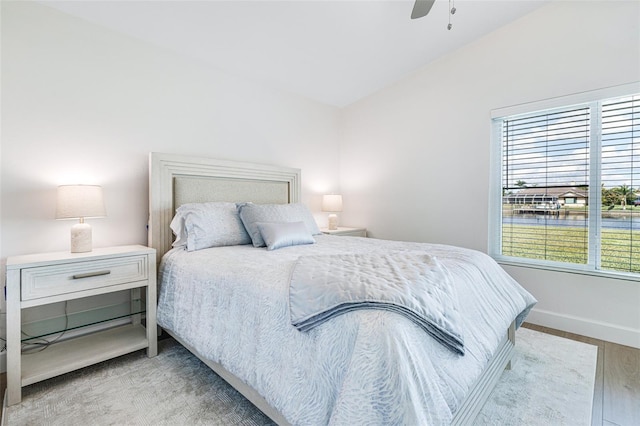 bedroom featuring light wood finished floors, ceiling fan, baseboards, and vaulted ceiling