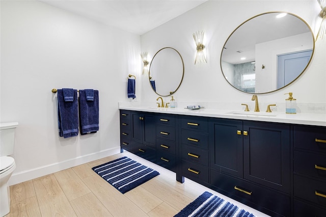 full bathroom featuring toilet, wood finished floors, a sink, baseboards, and double vanity