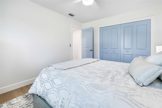 bedroom with wood finished floors, a ceiling fan, visible vents, baseboards, and a closet