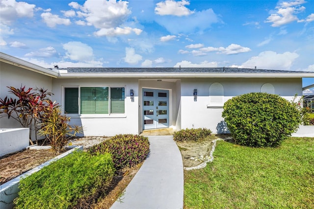 property entrance with french doors, a lawn, and stucco siding