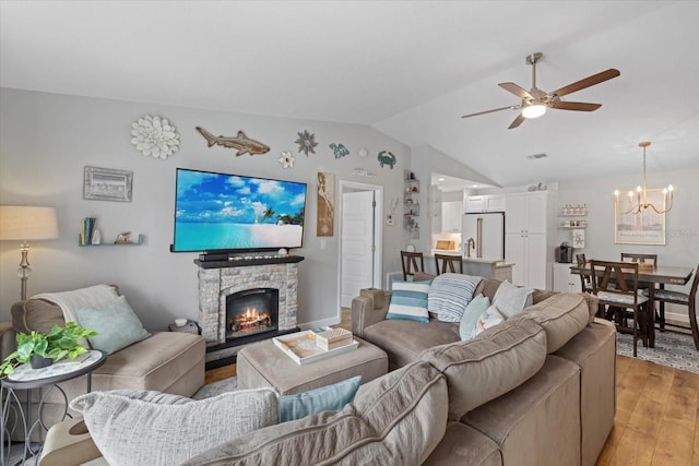 living room with light wood finished floors, visible vents, vaulted ceiling, a fireplace, and ceiling fan with notable chandelier