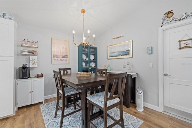 dining space featuring vaulted ceiling, a notable chandelier, light wood-style flooring, and baseboards