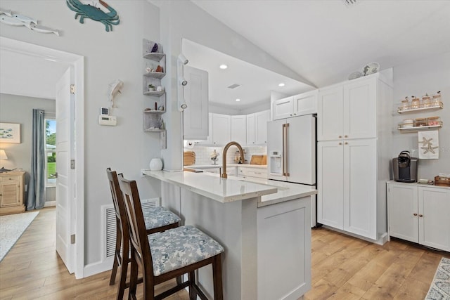 kitchen with high end white refrigerator, a peninsula, white cabinets, and a kitchen breakfast bar