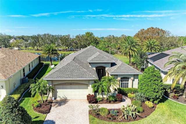 view of front facade with decorative driveway, roof with shingles, stucco siding, a front yard, and a garage