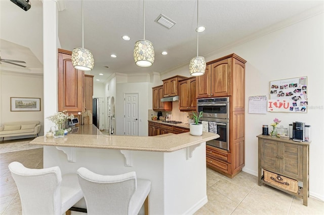 kitchen featuring white gas stovetop, visible vents, under cabinet range hood, double oven, and a kitchen bar