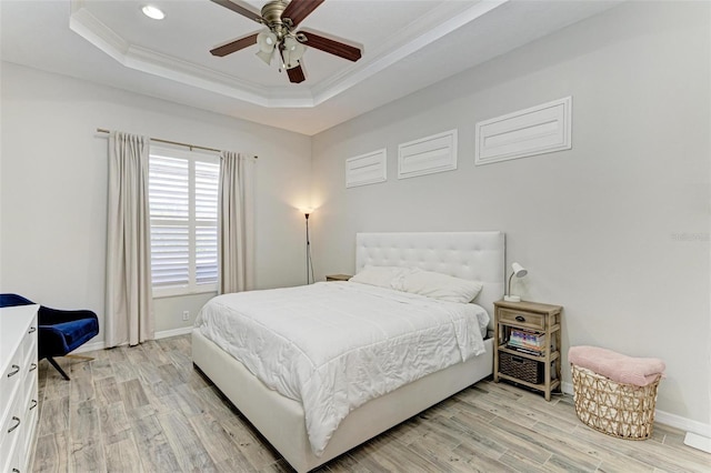 bedroom featuring baseboards, light wood-type flooring, a raised ceiling, and crown molding