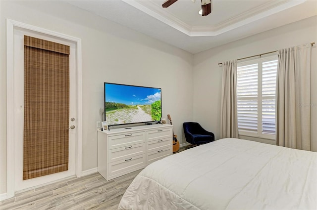 bedroom featuring light wood-style floors, a tray ceiling, ornamental molding, and ceiling fan