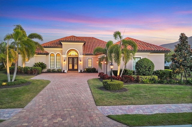 mediterranean / spanish-style house with decorative driveway, french doors, stucco siding, a lawn, and a tiled roof