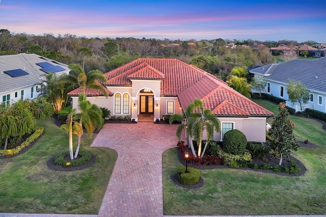 mediterranean / spanish-style home featuring decorative driveway, a tiled roof, french doors, and stucco siding