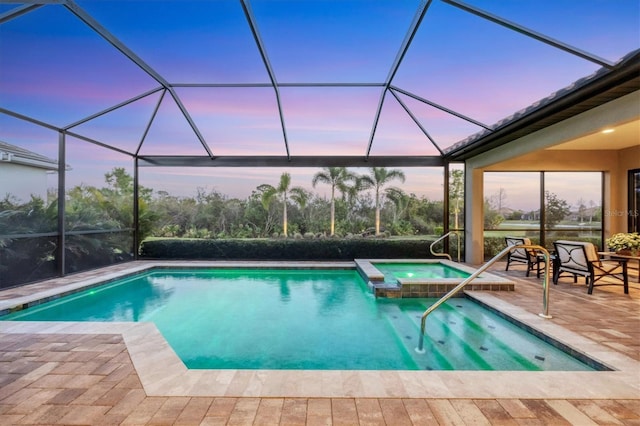 pool at dusk featuring a patio area, a pool with connected hot tub, and glass enclosure