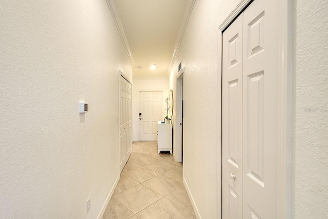 corridor featuring light tile patterned floors, crown molding, baseboards, and a textured wall