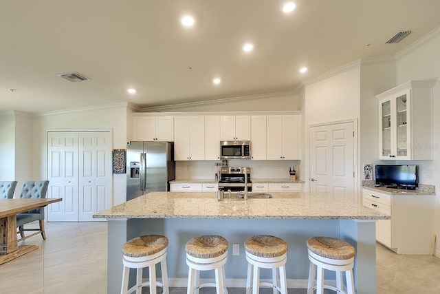 kitchen with visible vents, an island with sink, a sink, appliances with stainless steel finishes, and crown molding