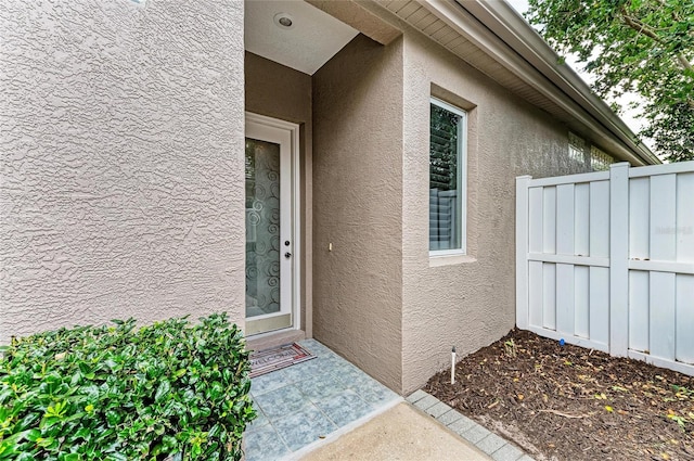 entrance to property featuring fence and stucco siding