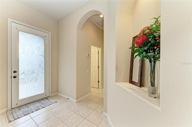 foyer entrance featuring arched walkways, light tile patterned flooring, and baseboards