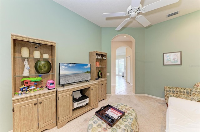 living area featuring arched walkways, light colored carpet, visible vents, ceiling fan, and baseboards